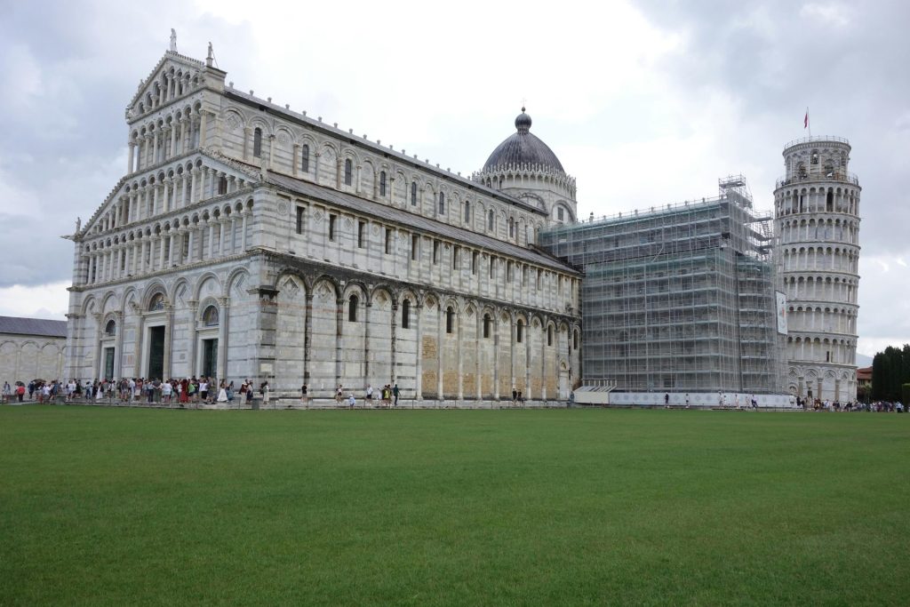 Blick auf den Dom von Pisa und den Schiefen Turm mit Gerüst unter bewölktem Himmel.