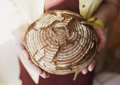 Eine Frau hält einen frisch gebackenen Laib Brot in ihren Händen und lächelt, während sie sich darauf vorbereitet, ihn zu teilen.
